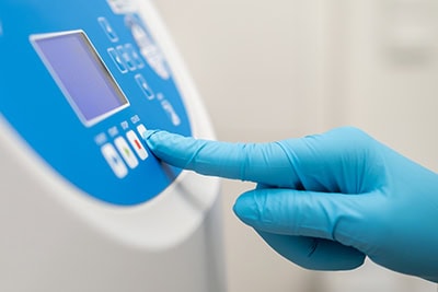 Close up laboratory worker hand in rubber gloves sets parameters on the centrifuge for sample preparation. DNA, oncology marker analysis in the clinical laboratory.